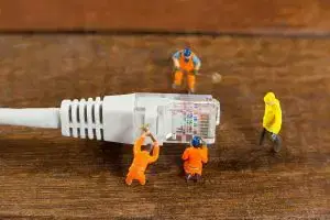 Miniature workers repairing an Ethernet cable, symbolizing IT support and network maintenance.