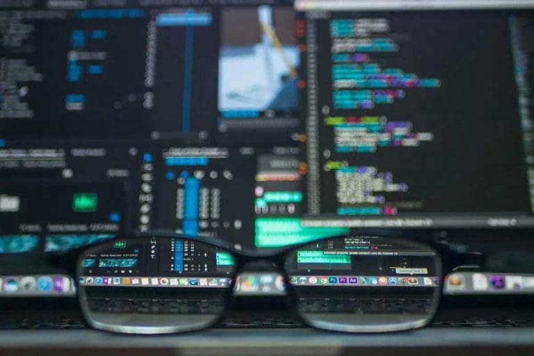 Essential Cyber Security Measures Every Business Needs 2 Computer screen with colorful code and system interfaces viewed through eyeglasses on a keyboard.